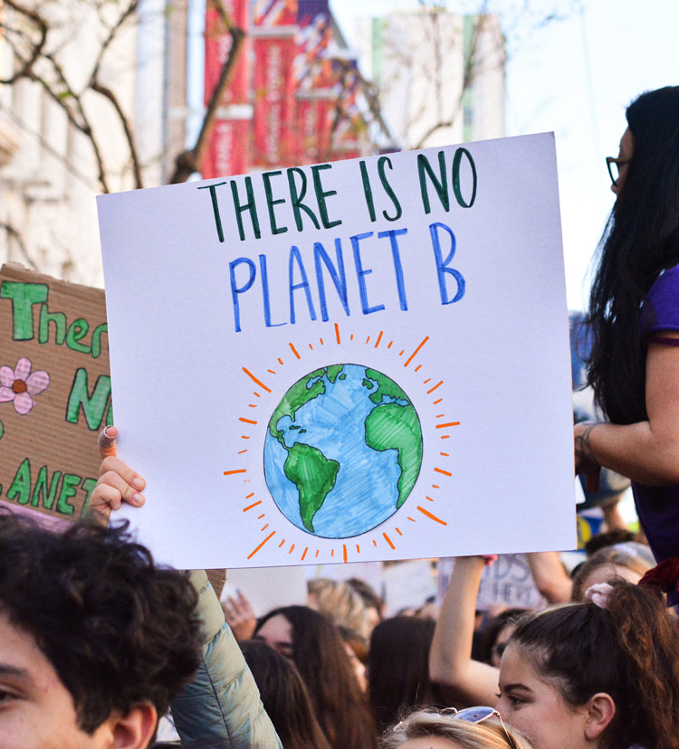 A sign is held up at an environmental protest. The sign reads "There is no Planet B" and has a drawing of the earth on it.