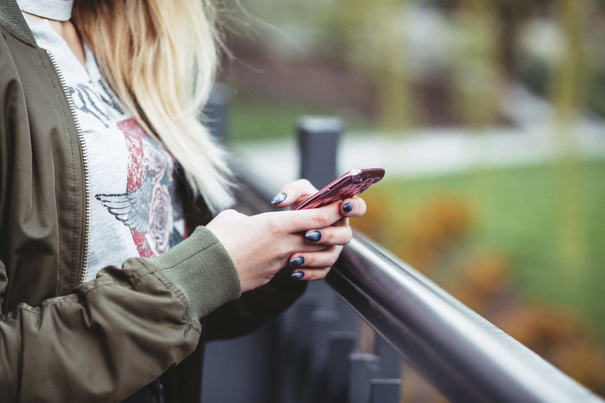 A person holding a red phone. We only see their torso and hands, which have painted nails. They're outside.